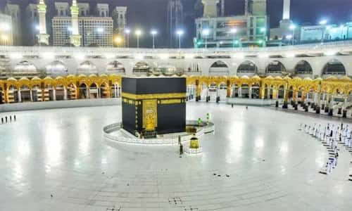 The black-draped Kaaba centered in the vast, empty white-tiled courtyard of the Grand Mosque in Mecca, surrounded by illuminated colonnades and buildings at night.